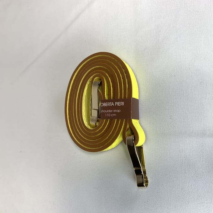 Ang dilaw na strap ng balikat na may gintong fittings ay nakapulupot at ang kayumanggi na label na "ROBERTA PIERI shoulder strap 110 cm" ay pinalamutian sa puting ibabaw.
