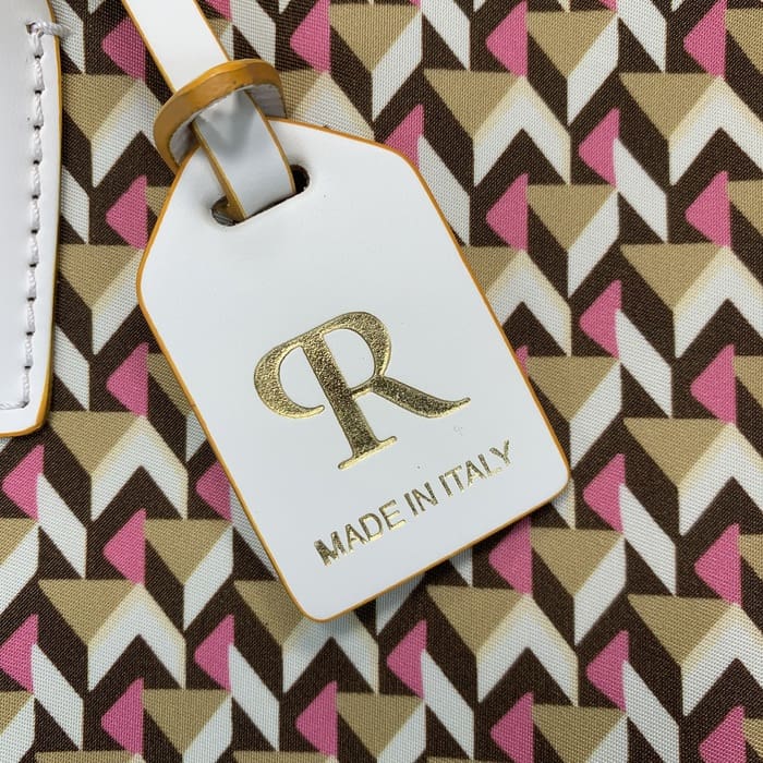 Isang close-up ng isang puting Roberta Pieri luggage tag na may titik na "R" sa ginto at ang mga salitang "MADE IN ITALY" na naka-attach sa isang mini duffel bag na nagtatampok ng brown, beige at pink geometric pattern.