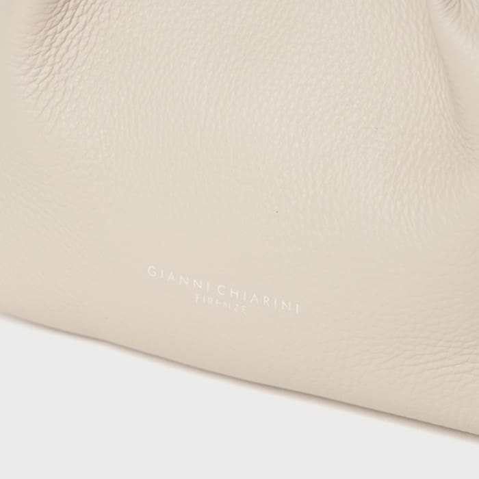 Isang close-up ng naka-texture na light beige leather surface na nagpapakita ng pino na pagkakayari ng Italyano na si Giannicchiarini. Malapit sa gitna ng ibaba, mayroong isang maliit na puting titik na naka-embossed na may mga salitang "GIANNI CHIARINI FIRENZE".